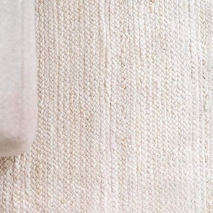 May include: A close-up of a white woven rug with a textured surface.
