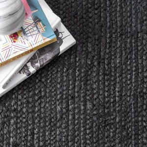 May include: Close-up of a black braided jute rug with a textured woven pattern. The rug is made of natural fibers and has a rustic look.