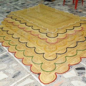 May include: A stack of five natural fiber rugs with scalloped edges. The rugs are layered with each rug having a different colored trim: red, green, black, pink, and white.