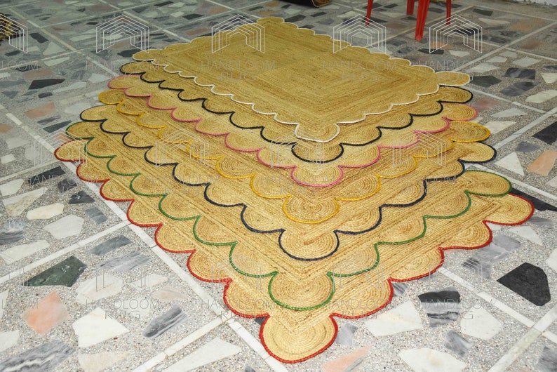 May include: A stack of five natural fiber rugs with scalloped edges. The rugs are layered with each rug having a different colored trim: red, green, black, pink, and white.