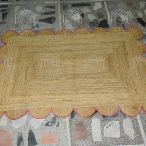 May include: A rectangular jute rug with a pink scalloped border. The rug is made of natural fibers and has a woven texture.