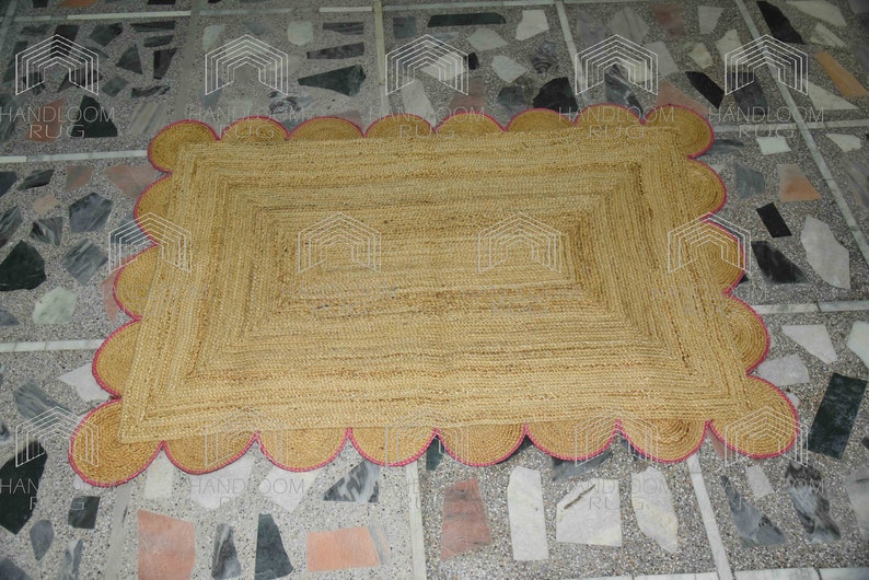 May include: A rectangular jute rug with a pink scalloped border. The rug is made of natural fibers and has a woven texture.