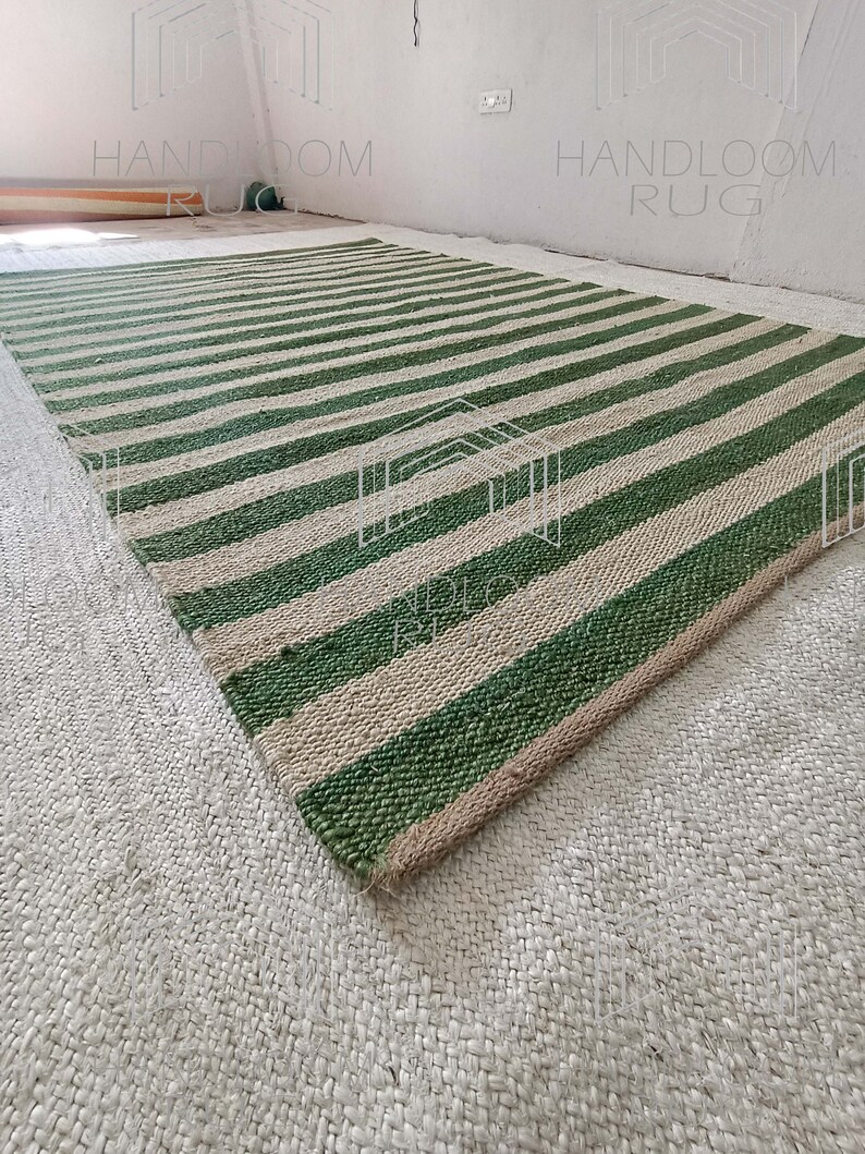 Op de afbeelding: Een groen en natuurlijk jute gestreept tapijt. Het tapijt is handgeweven en heeft een natuurlijke, rustieke uitstraling. Het tapijt is perfect om elke kamer een vleugje natuurlijke schoonheid te geven.