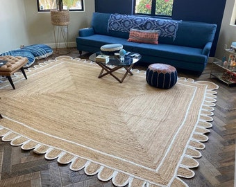 May include: A natural fibre rug with a white scalloped border. The rug is laid out on a dark wood floor in a living room setting with a blue sofa, a coffee table, and a pouf.