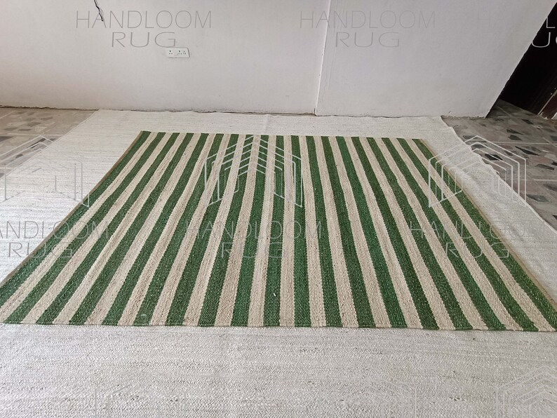 Op de afbeelding: Een handgeweven tapijt met groene en beige strepen. Het tapijt is gemaakt van natuurlijke vezels en heeft een rustieke uitstraling.