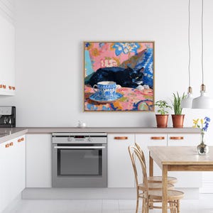 May include: A framed painting depicts a black cat resting on a floral patterned surface. A blue and white teacup and saucer sit in the foreground. The artwork features a vibrant color palette with pink, blue, and orange hues.