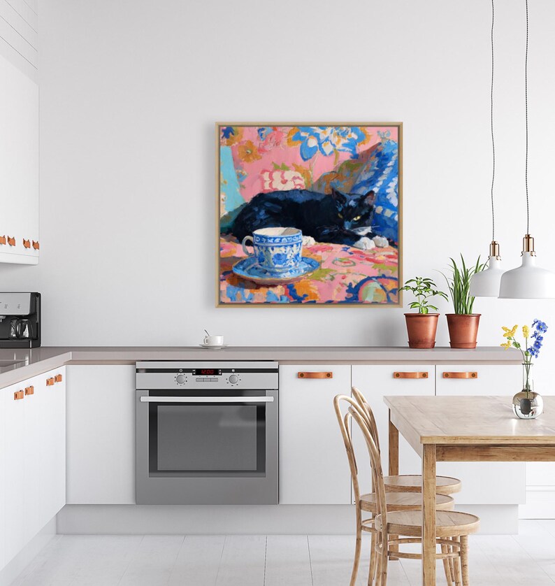 May include: A framed painting depicts a black cat resting on a floral patterned surface. A blue and white teacup and saucer sit in the foreground. The artwork features a vibrant color palette with pink, blue, and orange hues.