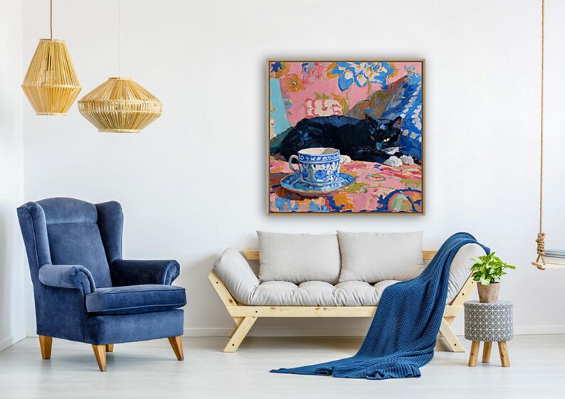 May include: An interior scene featuring a framed painting of a black cat resting on a floral patterned surface, with a blue and white teacup. A blue armchair, a wooden sofa, and a blue blanket are also visible.