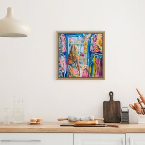 Puede incluir: Una pintura enmarcada representa a una mujer con un vestido floral colorido, de pie en un armario lleno de ropa vibrante. Un perro blanco peque&ntilde;o tambi&eacute;n est&aacute; en el armario. La obra de arte est&aacute; ambientada en una cocina con una l&aacute;mpara y una encimera de madera.