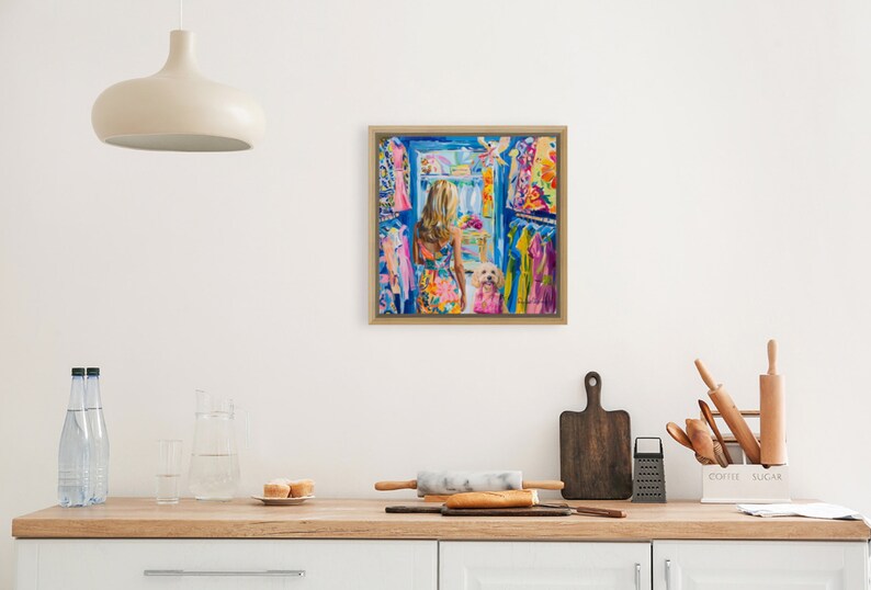 Puede incluir: Una pintura enmarcada representa a una mujer con un vestido floral colorido, de pie en un armario lleno de ropa vibrante. Un perro blanco peque&ntilde;o tambi&eacute;n est&aacute; en el armario. La obra de arte est&aacute; ambientada en una cocina con una l&aacute;mpara y una encimera de madera.