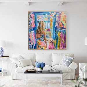 Puede incluir: Una pintura colorida representa a una mujer con un vestido floral mirando dentro de un armario lleno de ropa. Un perro con una camisa rosa est&aacute; a su lado. La obra de arte se exhibe sobre un sof&aacute; blanco en una sala de estar luminosa.