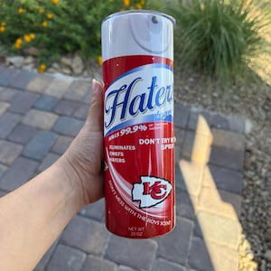 Pode incluir: Um copo isolado vermelho e branco com o texto "Hater" em uma fonte estilizada. O copo apresenta o texto "Kills 99,9%", "Eliminates Chiefs Haters" e "Don't Mess With The Boys Scent". O copo tem 591 ml.