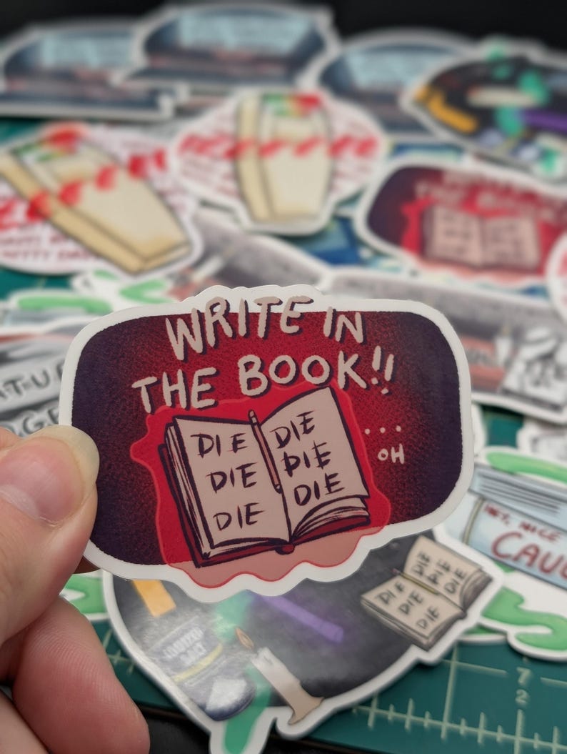 May include: A sticker with a red book that says "WRITE IN THE BOOK!!" and has the word "DIE" written on each page. The book is open and there is a pencil on the top page. The sticker is surrounded by other stickers.