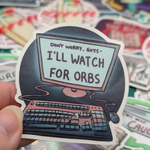 May include: A sticker with a cartoon illustration of a computer monitor and keyboard. The monitor screen displays the text "Don't worry, guys - I'll watch for orbs."