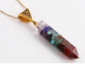 May include: A gold chain necklace with a seven chakra crystal pendant. The pendant is a clear, faceted, pointed crystal with layers of red, orange, yellow, green, blue, indigo, and violet crystals inside.