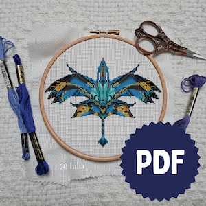 Peut inclure: Une broderie au point de croix d'un dragon stylisé dans un cercle à broder en bois. Le dragon présente des couleurs bleues, turquoise et dorées. Du fil à broder bleu et des ciseaux décoratifs sont également visibles. Un graphique PDF bleu foncé est dans le coin inférieur droit.