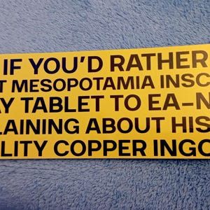 May include: A yellow rectangle sticker with black text. The text reads: "HONK IF YOU'D RATHER BE IN ANCIENT MESOPOTAMIA INSCRIBING A CLAY TABLET TO EA-NĀŞIR, COMPLAINING ABOUT HIS POOR QUALITY COPPER INGOTS."
