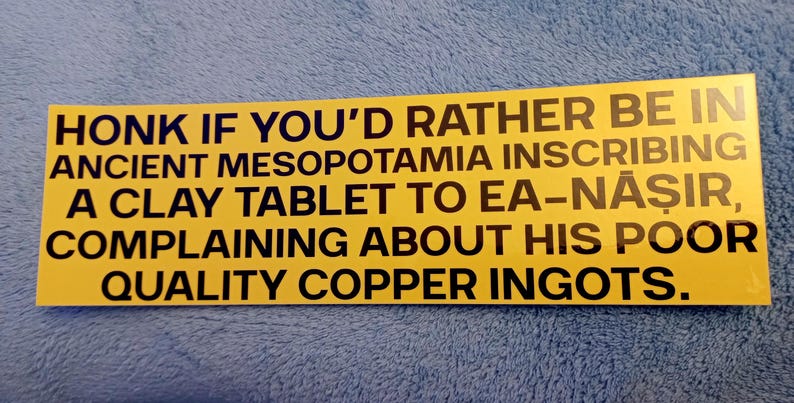 May include: A yellow rectangle sticker with black text. The text reads: "HONK IF YOU'D RATHER BE IN ANCIENT MESOPOTAMIA INSCRIBING A CLAY TABLET TO EA-NĀŞIR, COMPLAINING ABOUT HIS POOR QUALITY COPPER INGOTS."