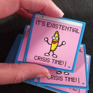 May include: A stack of stickers with a pink background and blue border. The top sticker features a pixelated banana character with the text "It's Existential Crisis Time!"