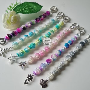 May include: Five colorful beaded keychains with different charms. The charms include a star, a crown, a flower, a lightning bolt, and a peace sign. The beads are ombre and have a pearl-like finish.
