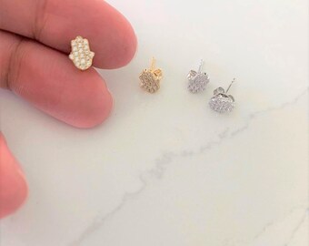 May include: Three pairs of hamsa hand earrings with cubic zirconia stones. The earrings are in gold, silver, and rose gold.