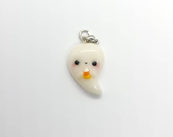 May include: A white ghost charm with a friendly face and a small orange and yellow candy corn in its hand. The charm is attached to a silver jump ring.