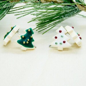 May include: A pair of Christmas tree earrings. One earring is green with gold glitter and the other is white with red and green glitter.