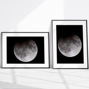 May include: Two black framed prints of a full moon in a dark sky. The moon is partially eclipsed, showing a darker shadow on the left side.