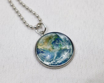 May include: A silver chain necklace with a round pendant featuring a detailed image of the Earth. The pendant has a silver rim and a clear glass cover.