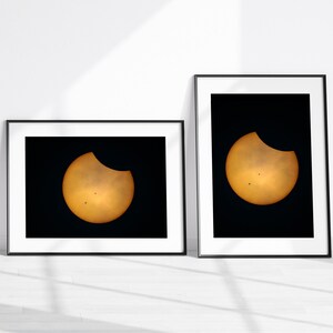 May include: Two framed photographs of a solar eclipse. The sun is partially obscured by the moon, creating a crescent shape. The photos are in black and white frames.
