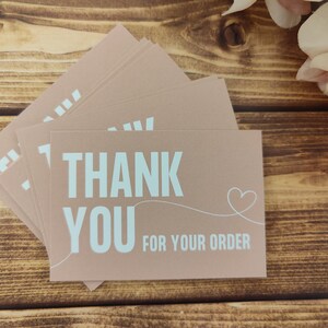 May include: A stack of thank you cards with a light brown background and white text that says "Thank You for your order" with a small heart drawn next to the text.