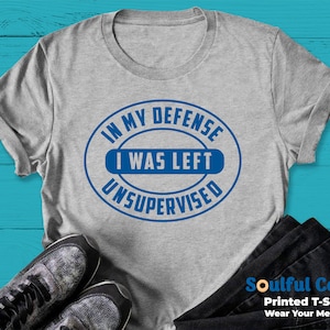 May include: A grey t-shirt with a blue circle graphic that says "In my defence I was left unsupervised".