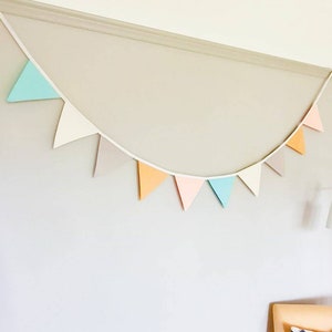 K&ouml;nnte beinhalten: Eine wei&szlig;e Schnur mit pastellfarbenen Dreiecksfahnen. Die Fahnen sind in den Farben hellblau, wei&szlig;, grau, orange, rosa und hellblau.