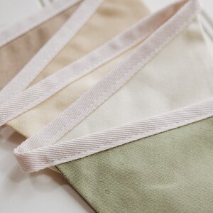 May include: A set of fabric pennants with a white, beige, and green color scheme. The pennants have a white trim around the edges.