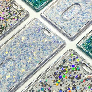 May include: A collection of rectangular clear plastic badge holders featuring liquid-filled interiors with floating glitter. Some holders contain fine iridescent blue and white glitter, while others feature larger, multi-colored hexagonal sequins.
