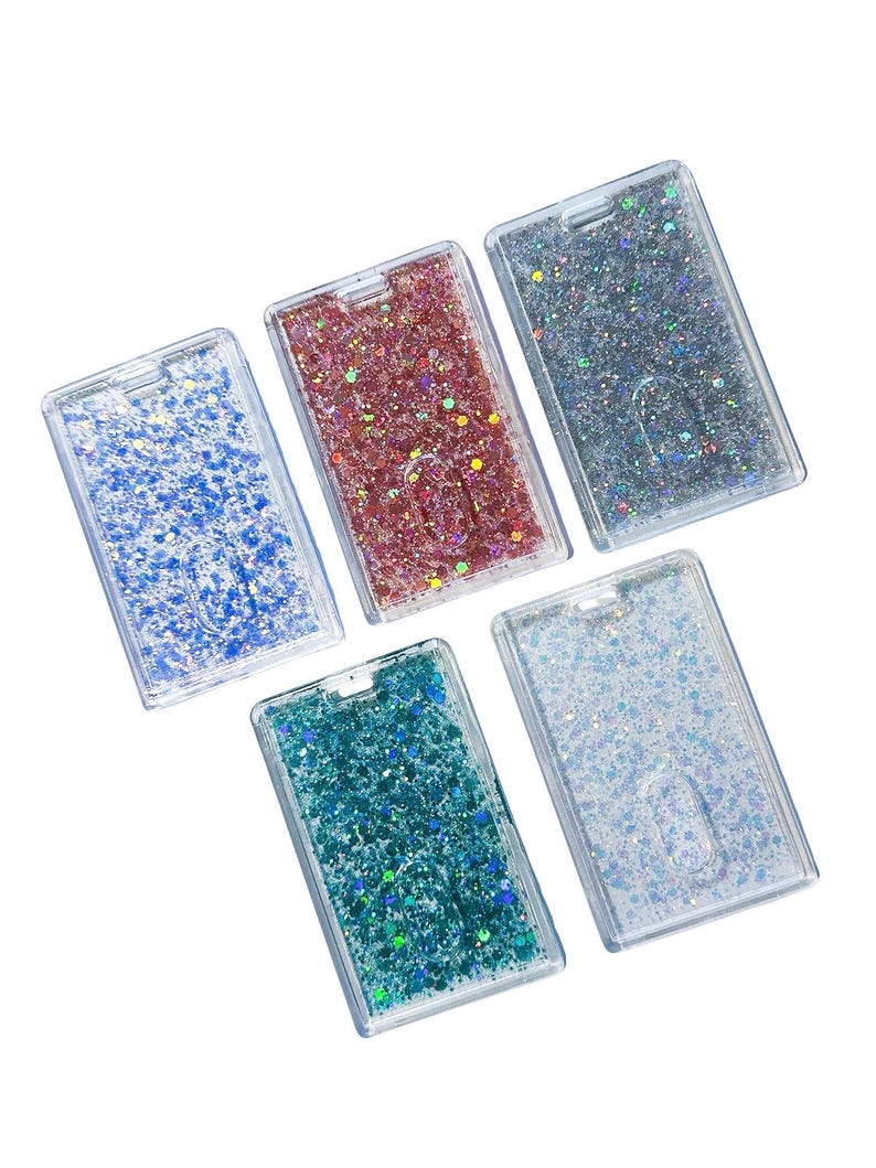 May include: Five rectangular plastic badge holders arranged in a cluster. Each holder features a clear frame filled with liquid and loose glitter in distinct colors: blue, pink, silver, teal, and iridescent white. Each has a slot for a lanyard.