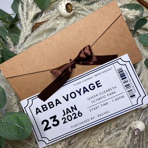 May include: A brown envelope tied with a brown ribbon, with a white ticket that reads "ABBA VOYAGE" for 23 January 2026, at Queen Elizabeth Olympic Park. The ticket includes a barcode and the text "PURCHASED BY: RACHEL."