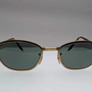 Puede incluir: Una taza de cerámica blanca con un asa negra y el texto "But First, Coffee" en negrita negra. La taza está sobre una superficie de madera. La taza mide aproximadamente 10 cm de alto.