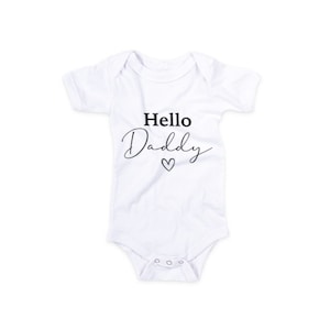 May include: White baby onesie with black text that reads "Hello Daddy" with a small heart symbol.