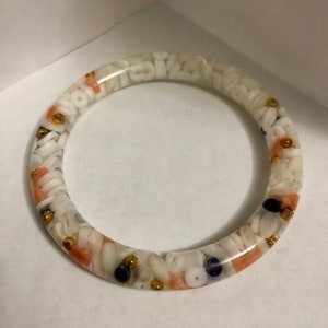 May include: White resin bangle bracelet with embedded white, pink, gold, and blue beads.