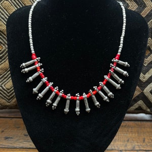 Könnte beinhalten: Eine silberne Halskette mit roten Perlen und silbernen Anhänger-Anhängern. Die Halskette wird auf einer schwarzen Samt-Mannequin-Büste präsentiert.