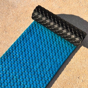 May include: A blue silicone rolling pin with a mermaid scale pattern. The rolling pin is rolled up and the end is visible.