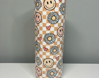 May include: A white tumbler with a checkered pattern in orange and white. The tumbler is decorated with smiley faces, daisies, and pink hearts.