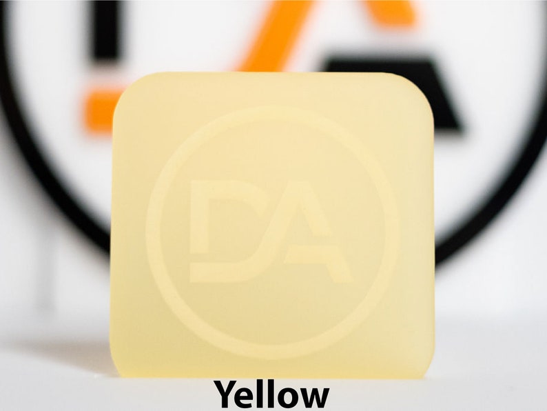 May include: A square, yellow object with rounded corners. The object has a circular logo with the letters "DA" inside. The word "Yellow" is printed at the bottom of the image.