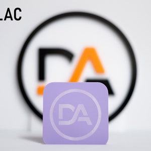May include: A lilac square business card with a white circle and the letters "DA" inside the circle.