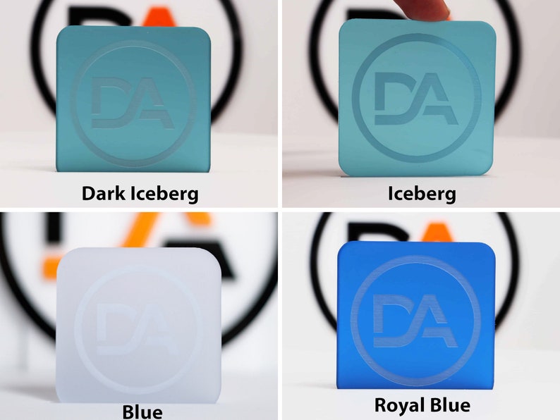 May include: Four square-shaped objects in various shades of blue and white are shown. Each square features a circular logo with the letters "DA" etched into the surface. The colours are labelled "Dark Iceberg", "Iceberg", "Blue", and "Royal Blue".