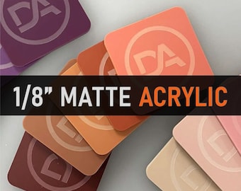 Könnte beinhalten: Ein Stapel mattierter Acrylquadrate mit einer Dicke von 1/8 Zoll, auf denen jeweils die Buchstaben "DA" in einem Kreis in der Mitte des Quadrats stehen. Die Quadrate sind in verschiedenen Brauntönen, Rosa und Lila.