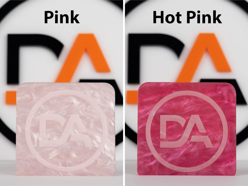 May include: Two square samples of acrylic plastic, one pink and one hot pink, with a white "DA" logo in a circle in the center of each.