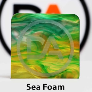 May include: A square, translucent chip with a swirling pattern of green and yellow. The chip has a white circle with the letters "DA" in the center.