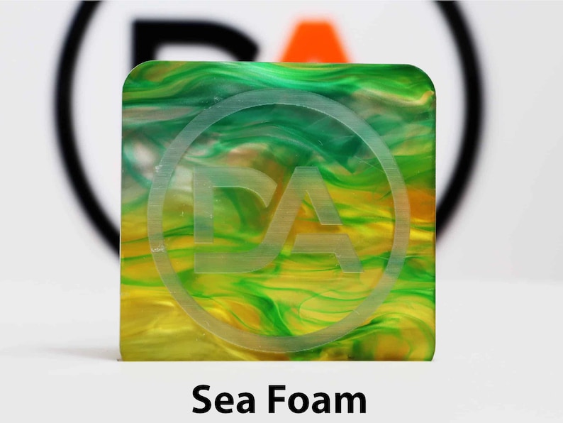 May include: A square, translucent chip with a swirling pattern of green and yellow. The chip has a white circle with the letters "DA" in the center.